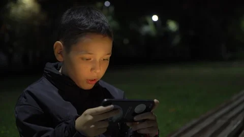 Active boy playing mobile game on the street at night, close up 库存影片 98877935
