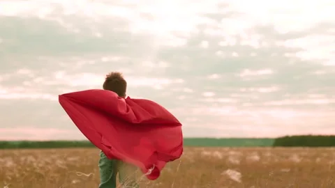 Active boy runs along field with growing plants with red cape behind back Stock Footage 254925698