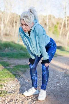 Active cheerful blonde pausing after a run in a park on a sunny day Stock Photos