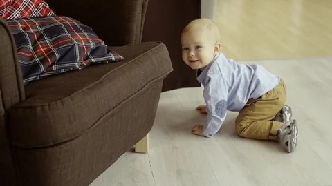 Active cheerful child crawls on the floor and laughs , hides behind a armchair Stock Footage 73718251