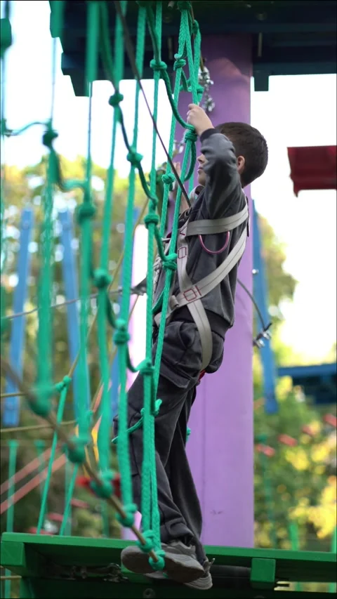 Active child enjoying a challenging rope course outdoors, climbing high  Stock Footage 345285416
