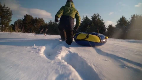 An active child runs through the snow, dragging a tubing behind him. Stock Footage 252807755