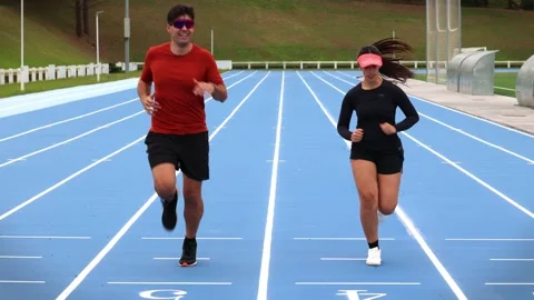 Active Couple of Runners Jogging Towards Camera on Outdoor Athletic Track Stock Footage 277500877