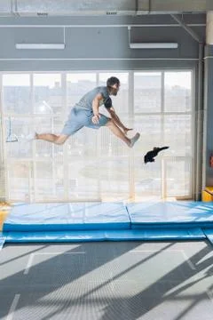 Active crazy guy is tryng to catch falling toy while jumping on the trampoline Stock Photos
