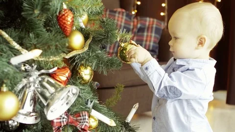 Active cute child plays with toy balls on a Christmas tree, in a cozy home Stock Footage 73718317