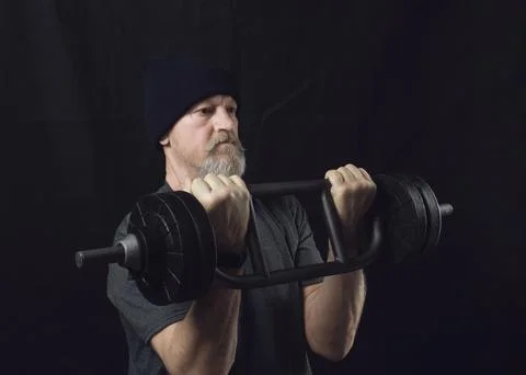 Active elderly man with a beard trains biceps with a barbell Foto stock