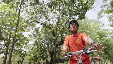 Active Elderly Man in Orange Cycling Gear Looking Up While Riding Bike Stock Footage 272217675