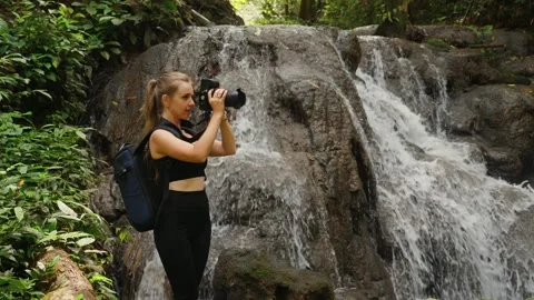 Active female photographer capturing waterfall scenery with camera. Nature Видео 260340700