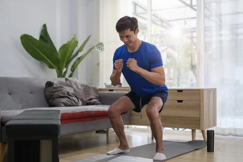 Active focused millennial man doing squat exercises at home. Sporty lifesty.. Stock Photos