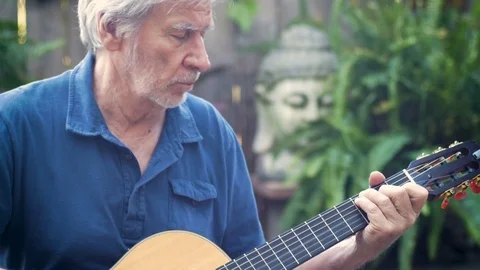 Active healthy senior man concentrating on playing acoustic guitar outdoors Stock Footage
