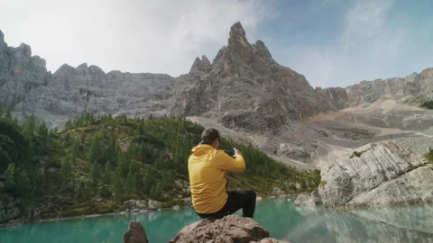 Active hiker in a yellow jacket standing on a rock overlooking Lago di Sorapis Video stock 320473607