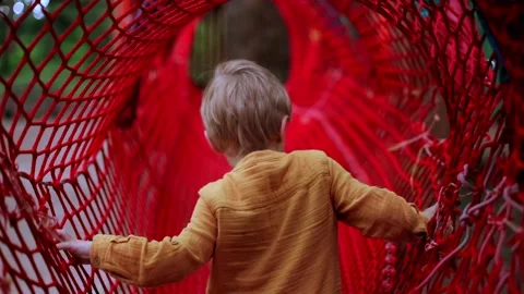 Active joyful little boy playing in red net on kids playground. Beautiful sunny Stock Footage 137957568