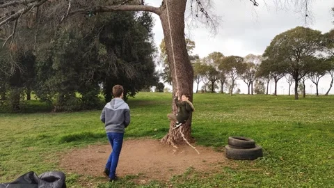 Active kid boy swing on homemade bungee on tree or have fun in city park outdoor Stock Footage 245086529