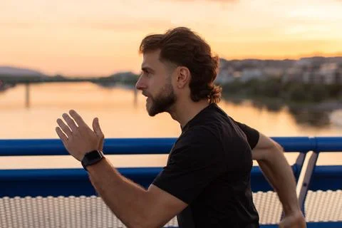 Active male runner training on city bridge at sunset, wearing sportswear and Stock Photos