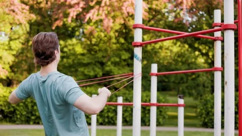 Active man does a fitness workout outdoors, using a resistance band for a back e Stock Footage 340280090