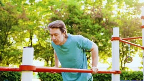 Active man doing calisthenics dips on parallel bars. Outdoor fitness workout and Stock Footage 337546365