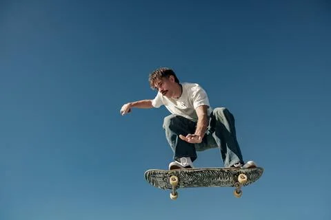 Active man doing tricks in the air on his skateboard at the skate park on blue Foto stock