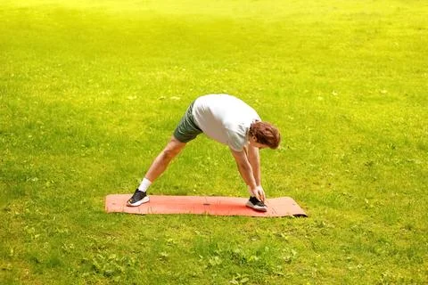 Active man doing yoga and stretching exercise on a mat outdoors in a green .. Stock Photos