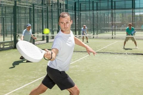 Active man engaged in padel in open-air court of tennis club Stock Photos