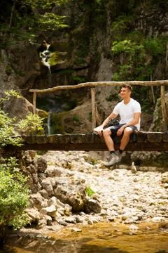 Active man resting on a bridge over mountain creek Stock Photos