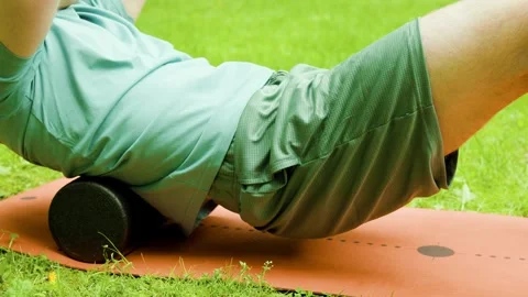 Active man uses a foam roller for myofascial back massage outdoors on the grass. Stock Footage 341971676