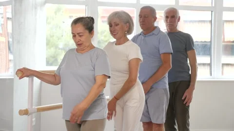 Active mature woman practicing basic positions in group holding by ballet barre Stock Footage 326316031