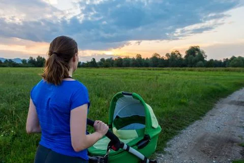 Active mom pushing a stroller at sunset. Stock Photos