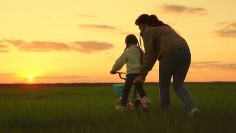 Active mother teaches child to keep balance while sitting on bicycle. Childhood Stock Footage 212348801