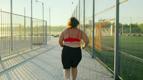 Active obese female jogging along the sports fence for morning fitness. Video stock 344249355