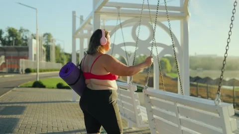 Active obese female resting by the park swing holding her purple fitness mat. Stock Footage 344249396