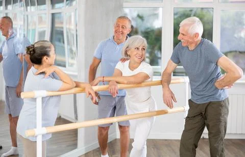 Active old attendees of ballet courses communicating cheerfully at ballet-barre 스톡 사진