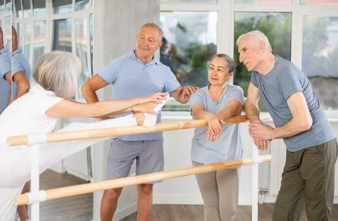 Active old attendees of ballet courses communicating cheerfully at ballet-barre 스톡 사진