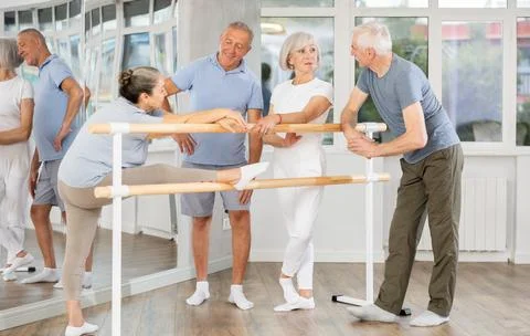 Active old attendees of ballet courses communicating cheerfully at ballet-barre 스톡 사진