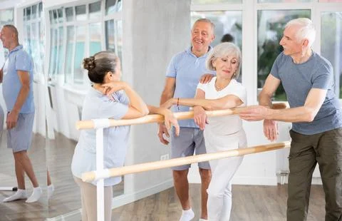 Active old attendees of ballet courses communicating cheerfully at ballet-barre 스톡 사진