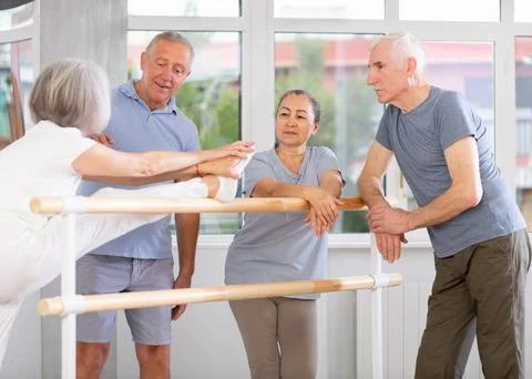 Active old attendees of ballet courses communicating cheerfully at ballet-barre Stock Photos