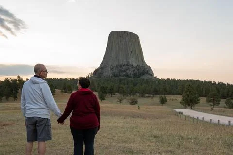 An active retired couple stand with backs to the camera looking at Devils Tower Stock Photos