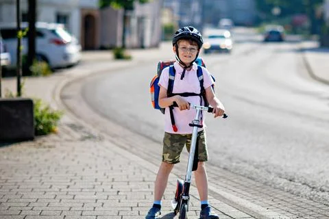 Active school kid boy with glasses in safety helmet riding with his scooter in Stock Photos