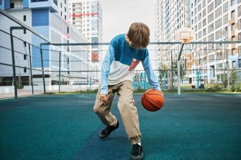 Active secondary school learner in pants and pullover playing basketball Stock Photos