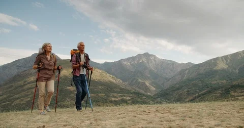Active senior caucasian couple hiking in mountains with backpacks, enjoying Stock Footage