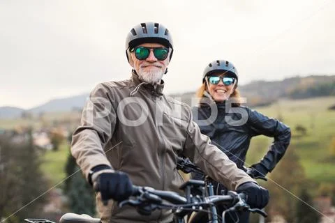 Active senior couple with electrobikes standing outdoors on a road in nature. Stock Photos