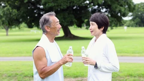 Active Senior Japanese Couple Drinking Water and Talking in Green Park Stock-Footage 344012469