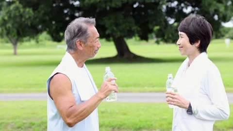 Active Senior Japanese Couple Drinking Water and Talking in Green Park 스톡 동영상 344012504