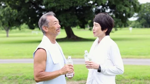 Active Senior Japanese Couple Drinking Water and Talking in Green Park Stock-Footage 344012645