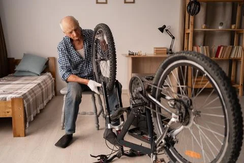 Active senior man adjusting bicycle wheel and chain at home. Bike repair, diy Фото