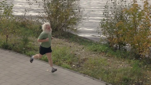 Active senior man in sport wear with gray hair running along pavement Видео 117291953