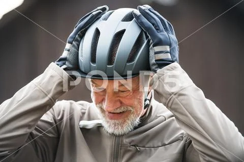 An active senior man standing outdoors in town, putting on a bike helmet. Stock Photos