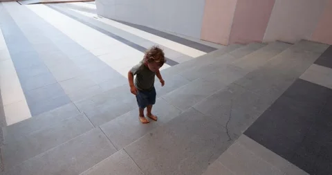 Active toddler jumping up and down stone stairs at building passage Stockbeeldmateriaal 345804070