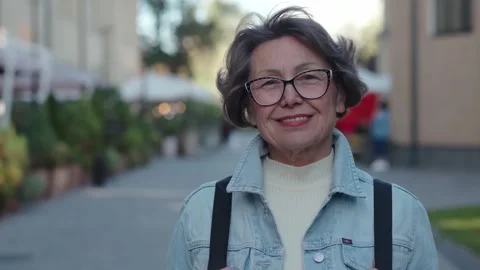 Active tourist an elderly lady with rucksack behind on city park background Stock Footage 257093658