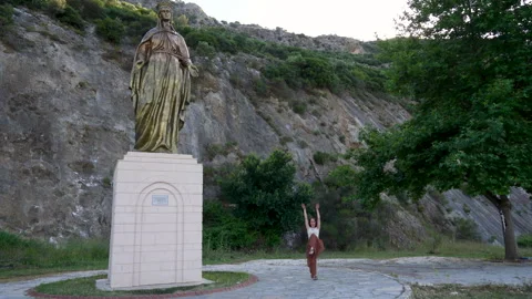 Active woman doing an athletic split jump dance near the Virgin Mary monument Stock Footage 336040492