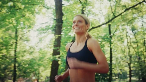 Active woman jogging through green park on sunny day Stock Footage 318411310